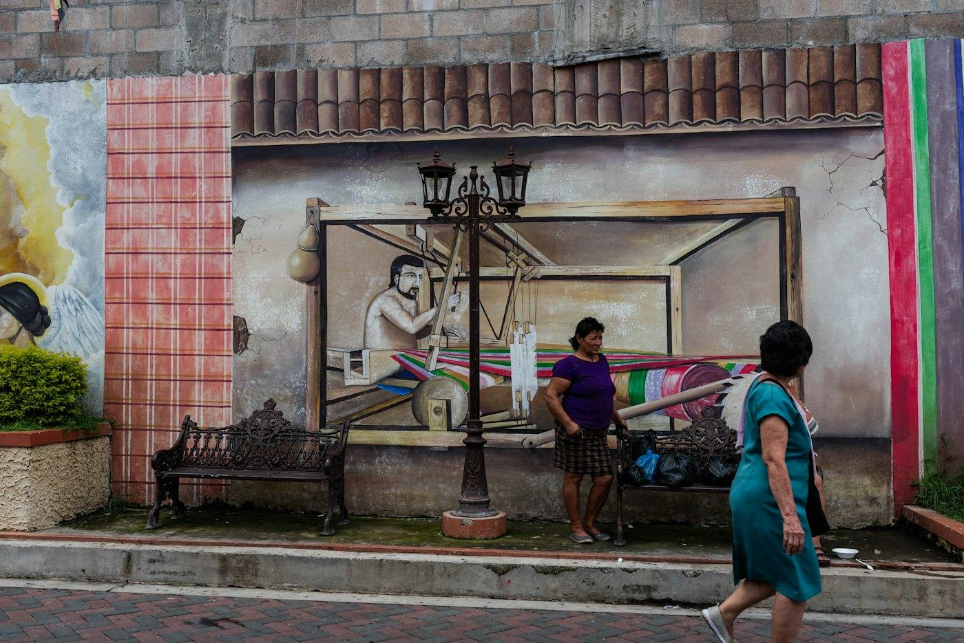 Mujeres caminando frente a un mural del telar en San Sebastián
