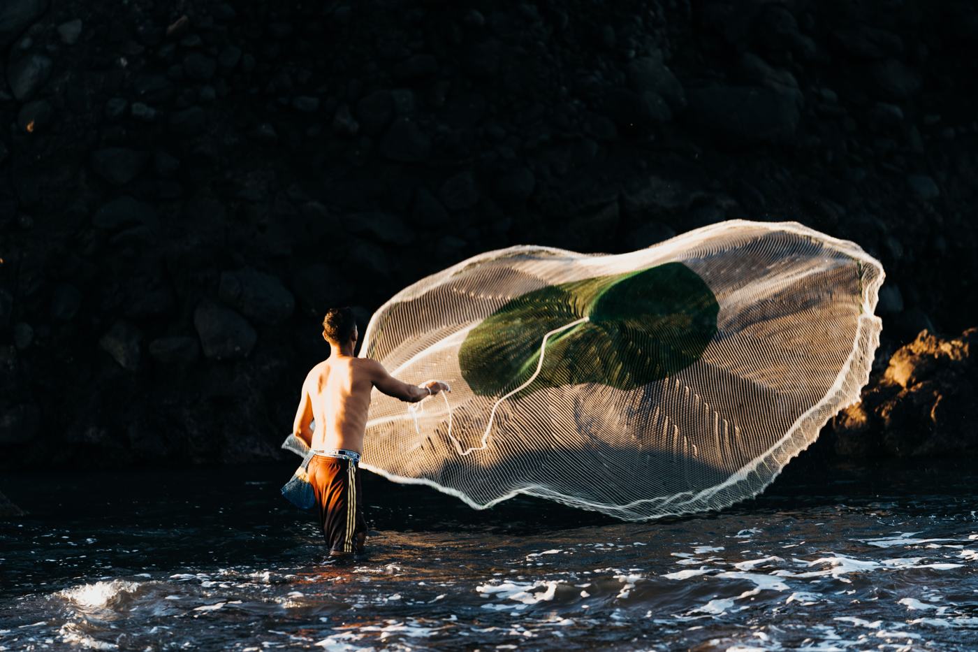 Pescador salvadoreño lanzando su atarraya al atardecer en la playa El Tunco